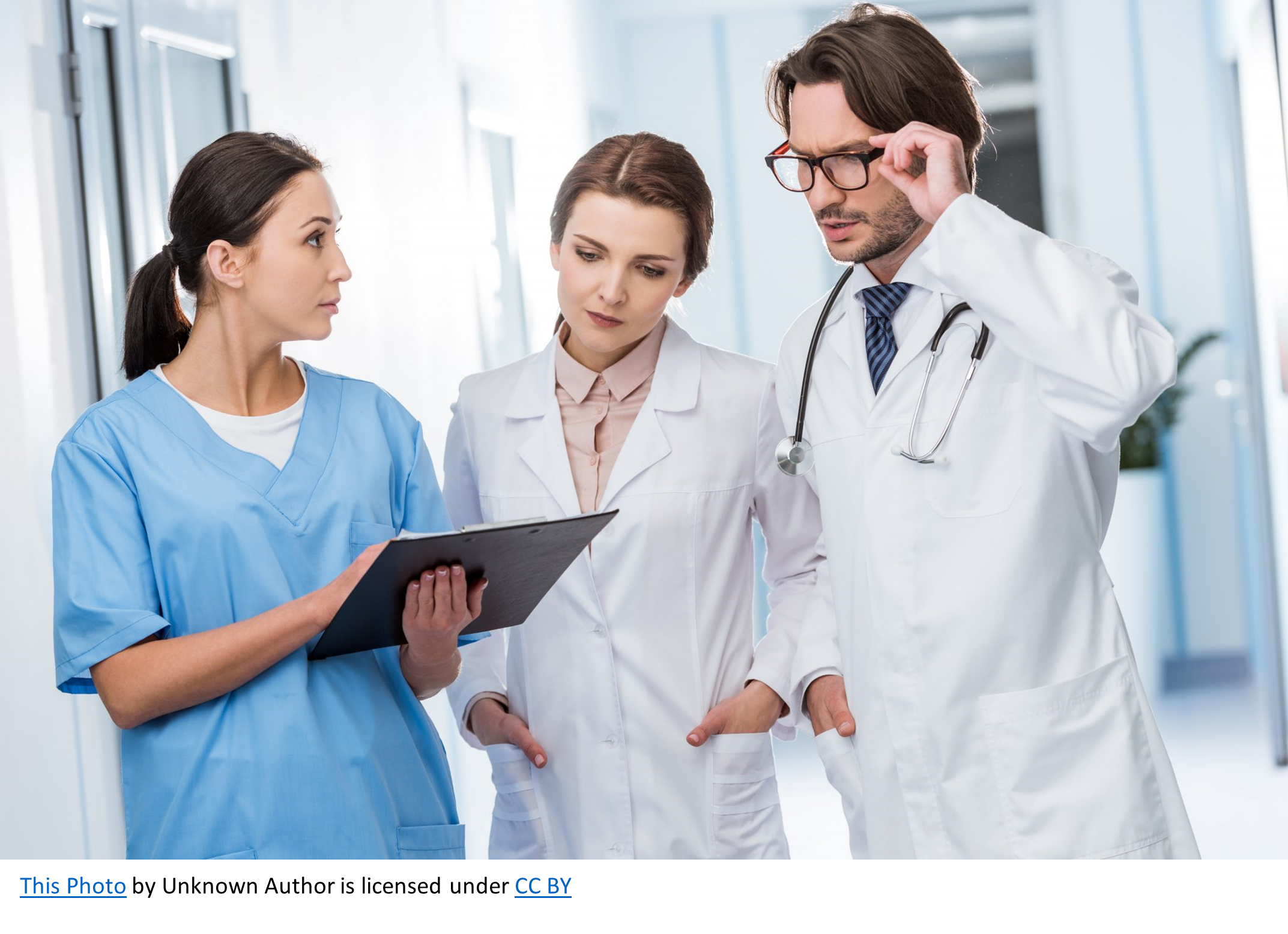 Three medical professionals stand in a hospital hallway engaged in discussion. The scene reflects teamwork and professional communication in a clinical setting.