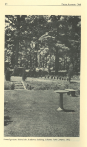Black and white photo of a landscaped formal garden behind the Academic Building at Montgomery College’s Takoma Park Campus in 1952. The scene includes trimmed hedges, a stone stairway, a circular birdbath or garden feature, and dense woods in the background.