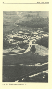 Aerial black and white photograph of the Germantown Campus in 1977, surrounded by open fields and forested areas, with a few academic buildings, curved roads, and parking lots visible.