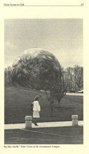 A woman stands on a paved area looking toward the “Big Blue Marble” water tower at Montgomery College’s Germantown Campus. The spherical tower is painted to resemble planet Earth and rises above a grassy slope and trees.