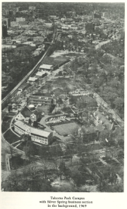Black-and-white aerial photograph taken in 1969 showing Montgomery College’s Takoma Park Campus in the foreground, including academic buildings, parked cars, and tree-lined roads. In the background, the dense commercial area of downtown Silver Spring stretches toward the horizon.